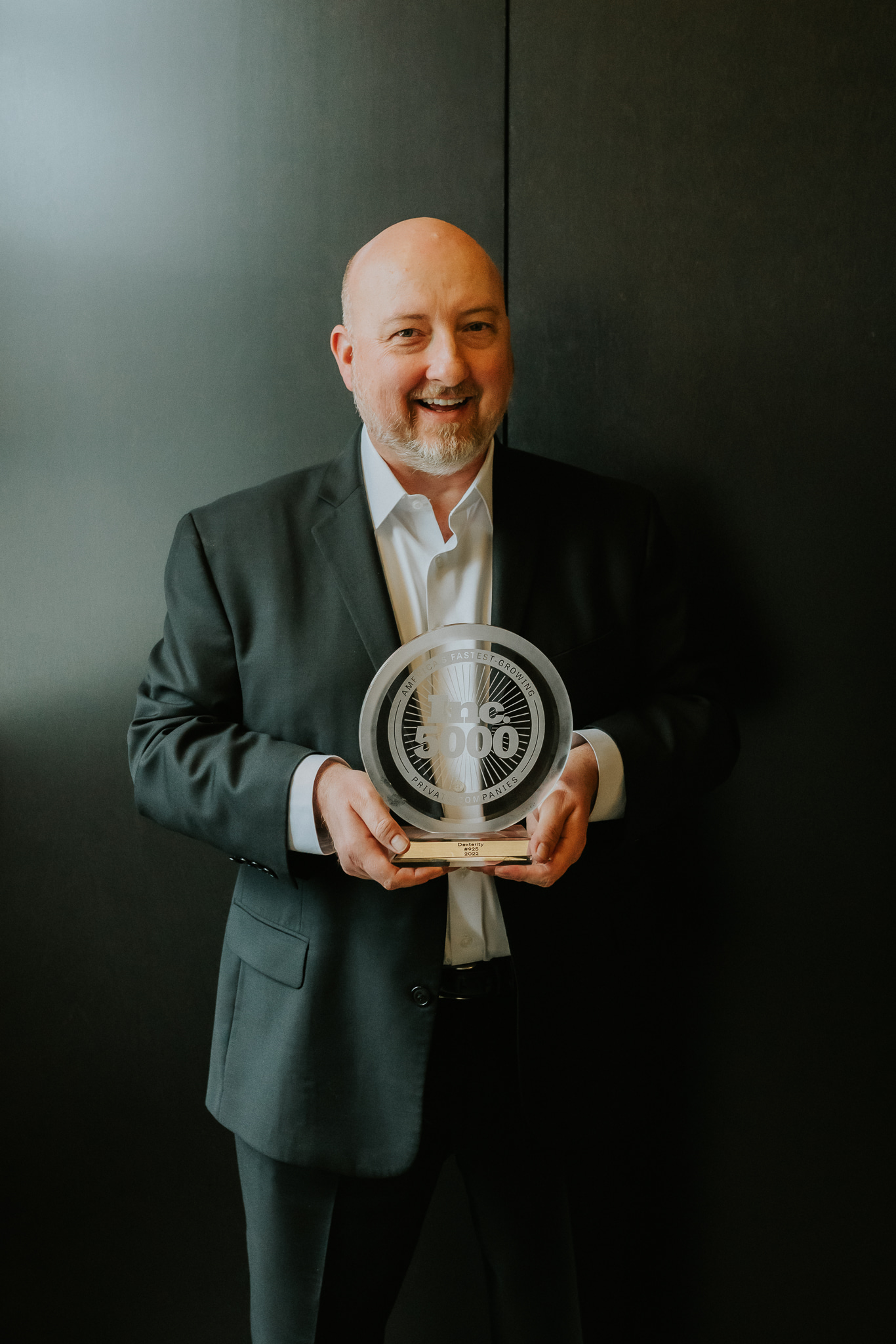 Dexterity founder Matt West dressed in a sport coat and button down holds a circular glass award for making the Inc. 5000 list