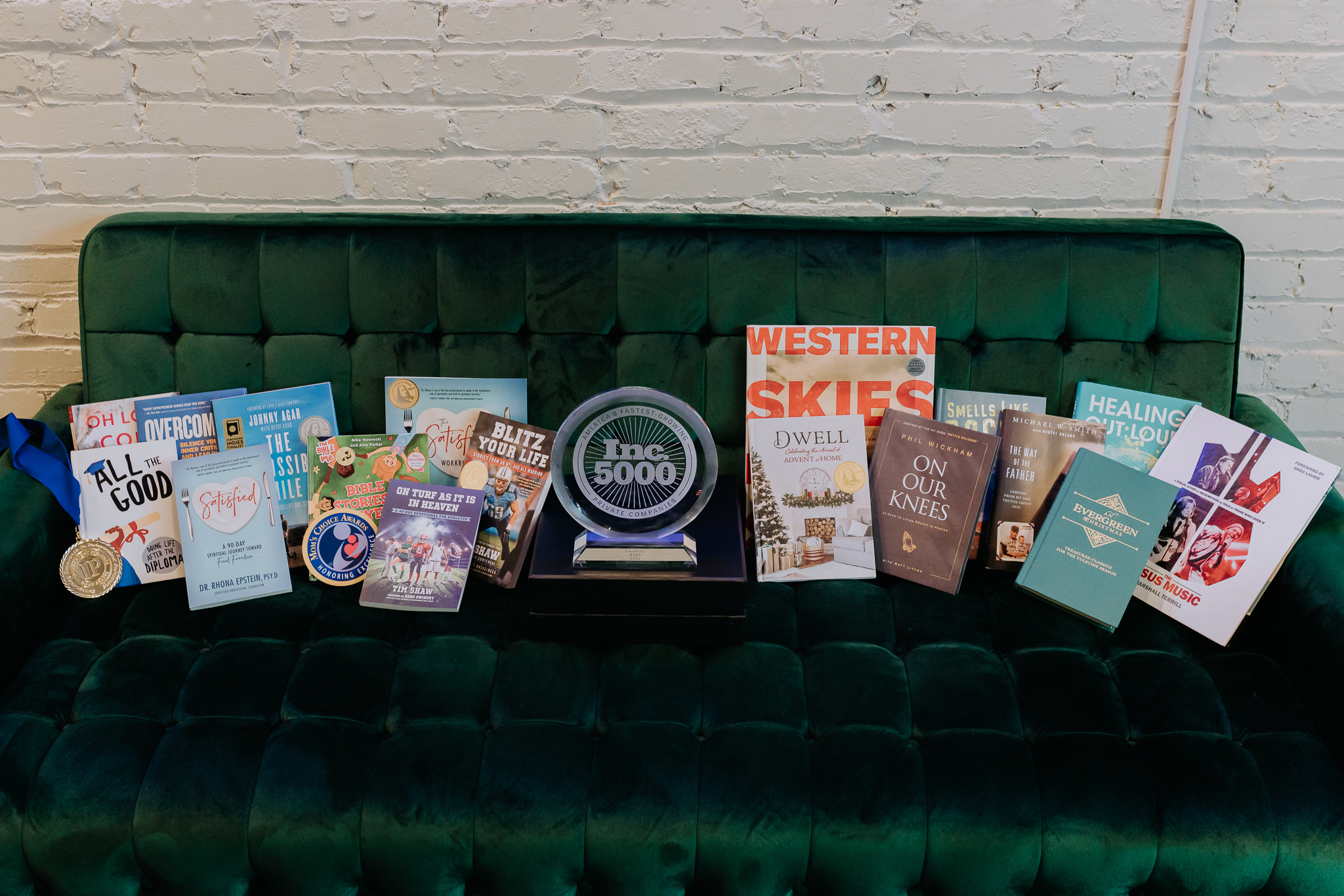 green velvet couch holds a variety of Dexterity published books and a circular glass award for INC. 5000
